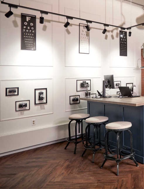 Eye charts and framed vintage cameras above the stools at the dispensing bar